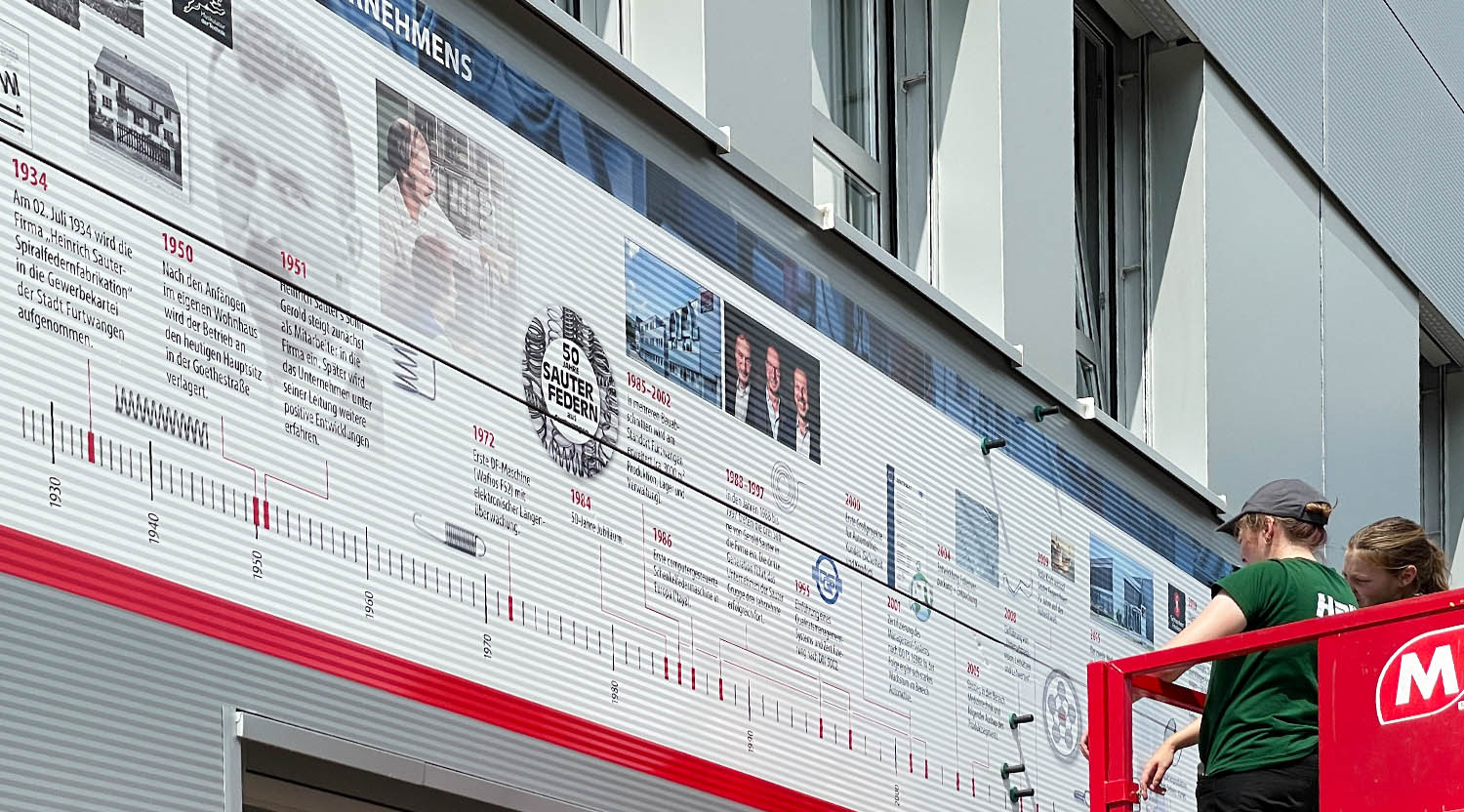 Sauter Federn: Anbringung eines riesigen, visuellen Zeitbands der neunzigjährigen Unternehmensgeschichte auf die Fassade des Unternehmens